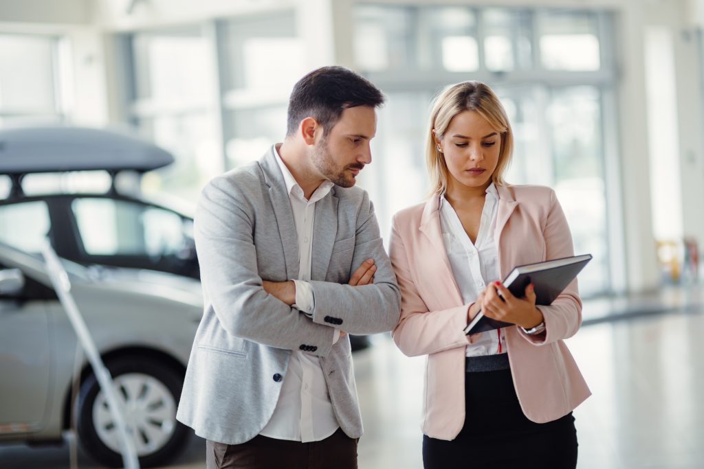 Mujer dando un speech de ventas a un hombre que quiere comprar un automóvil.